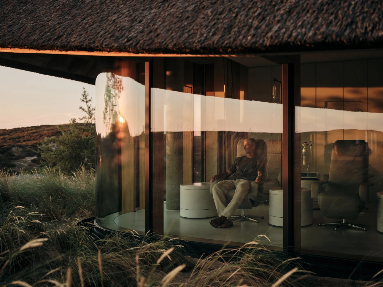 Pavilhão de vidro entre as dunas do Lanserhof Sylt ao pôr do sol.